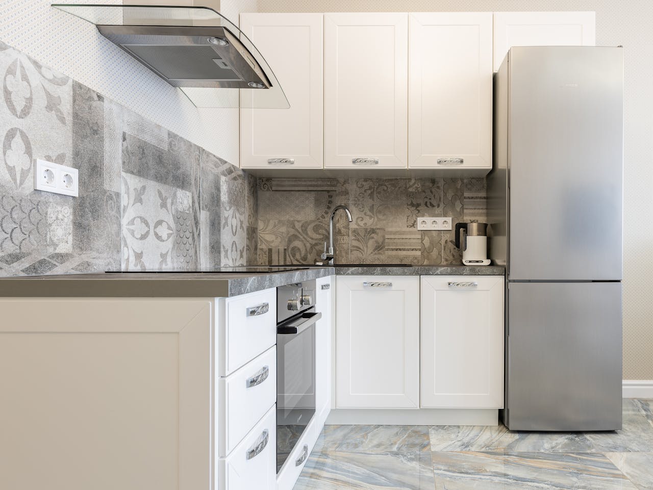 Modern kitchen interior with white cabinets and fridge against electric kettle and ornamental wall in light house